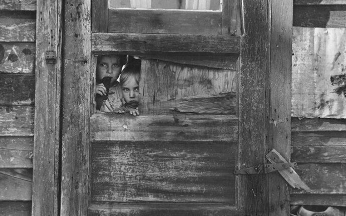 Black And White Photo Of Children Peeking Through A Door